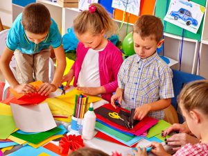 Kids holding colored paper on table in kindergarten